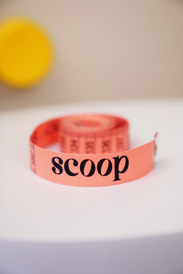 A Scoop measuring tape coiled on a table, marked in inches and centimetres